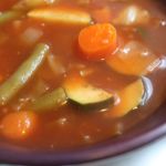 Bowl of soup containing carrots, zucchini, cabbage and green beans