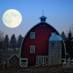 A scene at dusk, with a large moon on the left and a red barn and silo in the foreground
