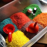 large plastic bin full of six piles of colored rice: blue, red, green, yellow, purple and orange