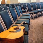 A long row of church chairs with a guitar lying across three of them