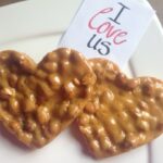 Two heart-shaped peanut brittle “cookies” on a white plate with a note that reads, “I love us.”