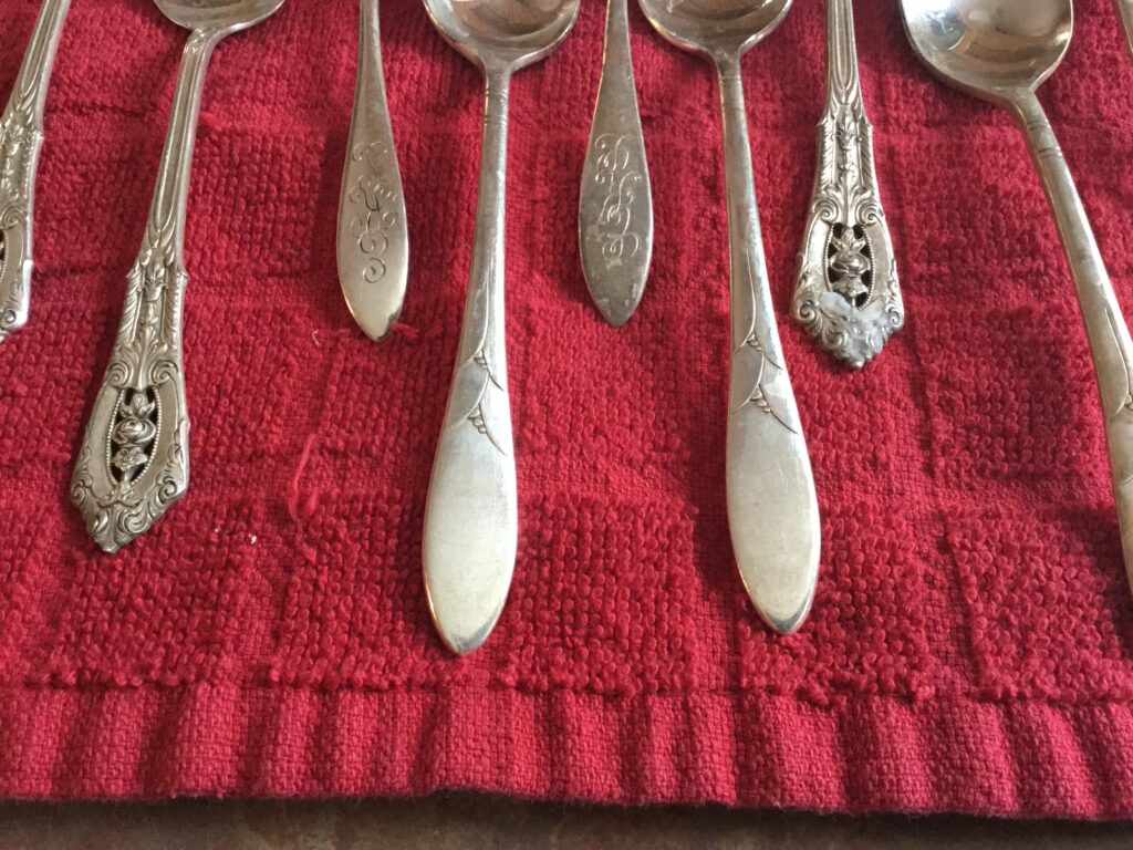 The bottoms of eight silver spoons set out on a red cloth