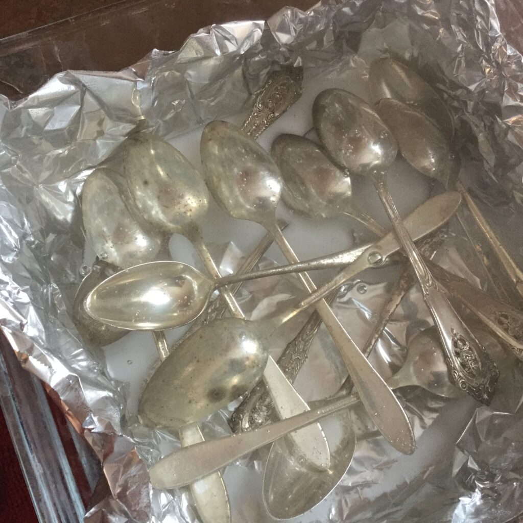Silver spoons laid out on foil-lined pan with baking soda an water
