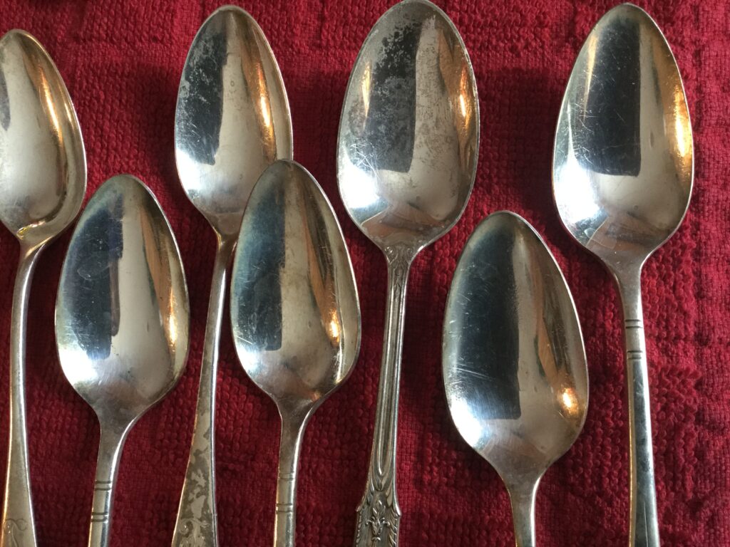 Seven silver spoons laid out on a red cloth