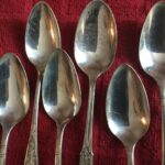 Seven silver spoons laid out on a red cloth