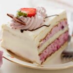 Piece of vanilla frosted wedding cake with a swirl of frosting and a strawberry on top